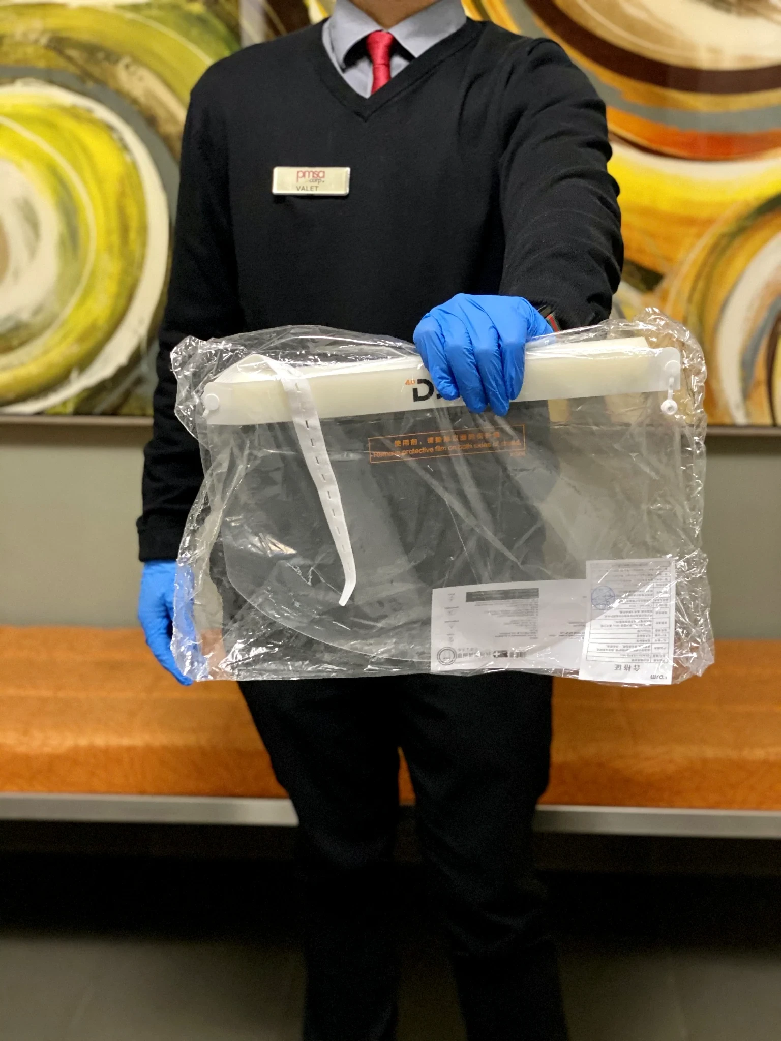 PMSA attendant in uniform holding a packaged face shield in front of colorful artwork