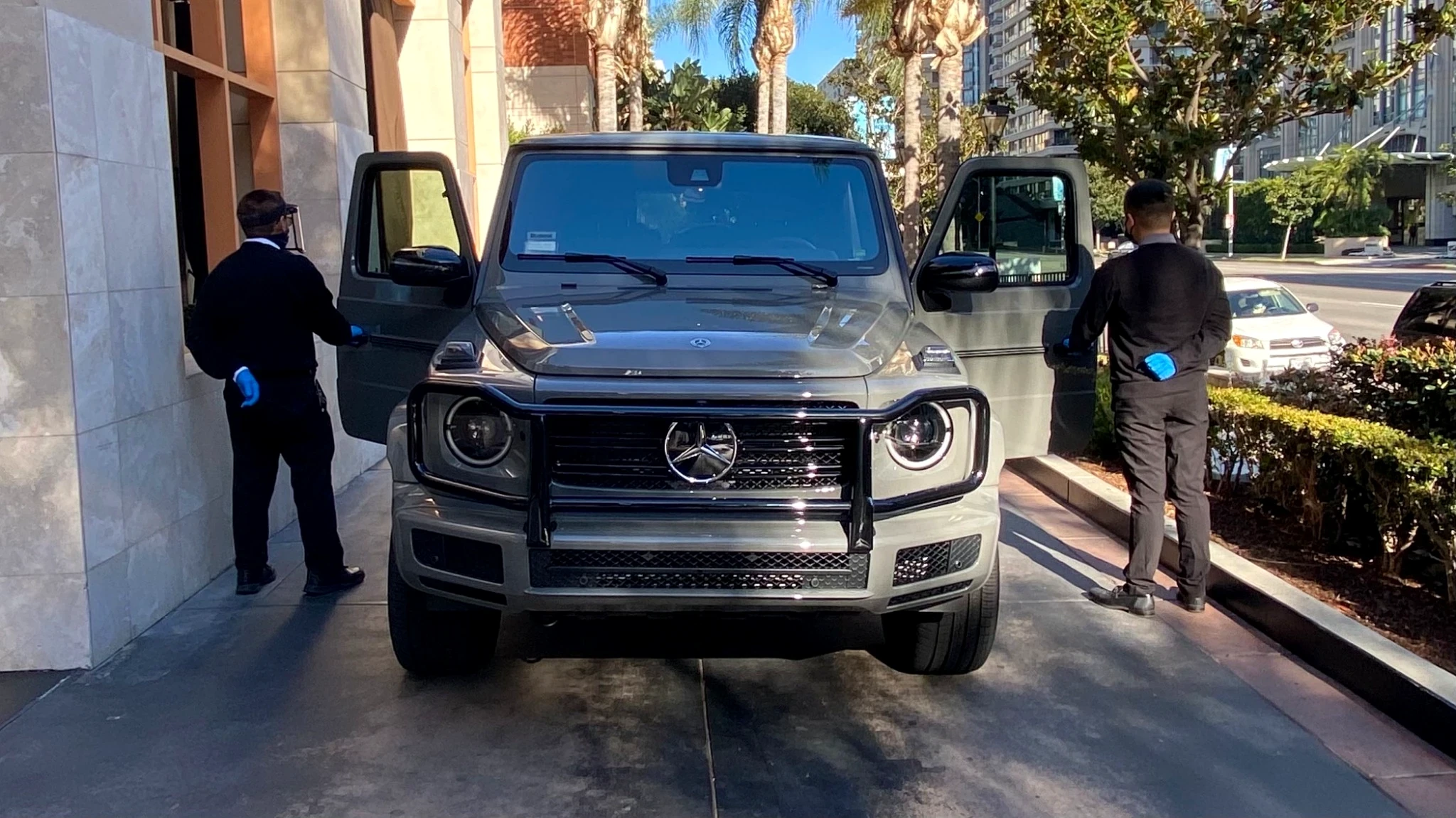 Two PMSA attendants simultaneously opening both doors of a Mercedes G-Wagon at a luxury hotel entrance