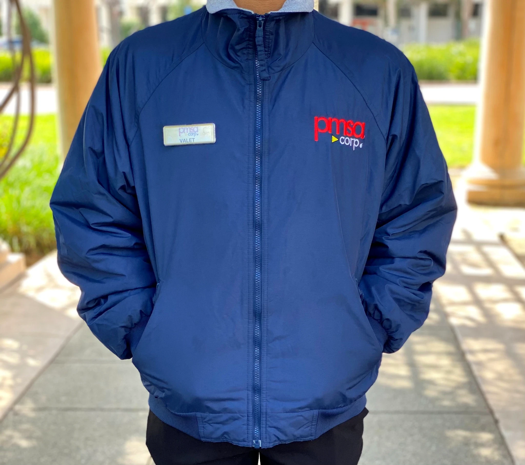 PMSA branded navy windbreaker jacket with valet name badge at an outdoor colonnade