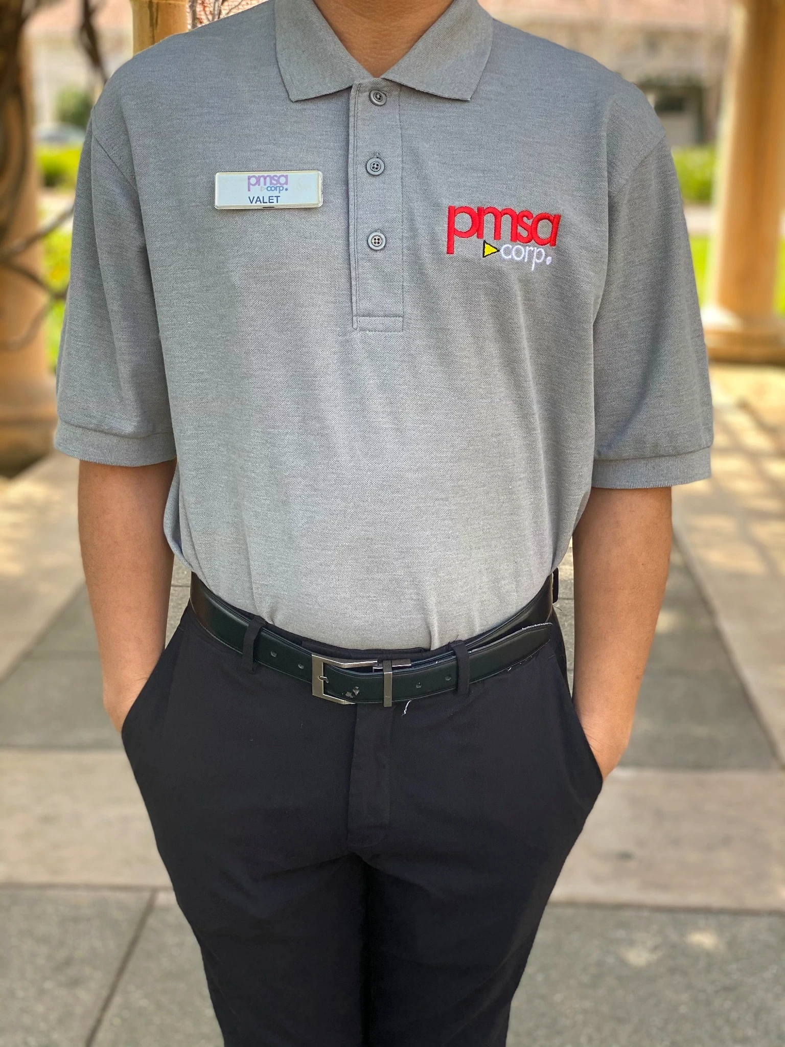 PMSA attendant in grey polo shirt, valet badge, and black slacks at an outdoor colonnade
