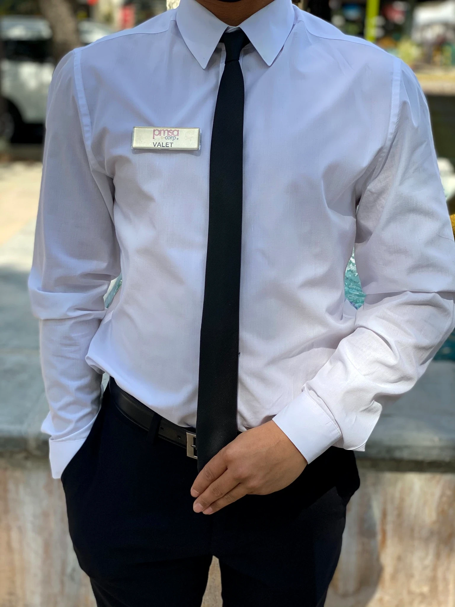 PMSA attendant in white dress shirt, black tie, and valet badge at an outdoor street setting