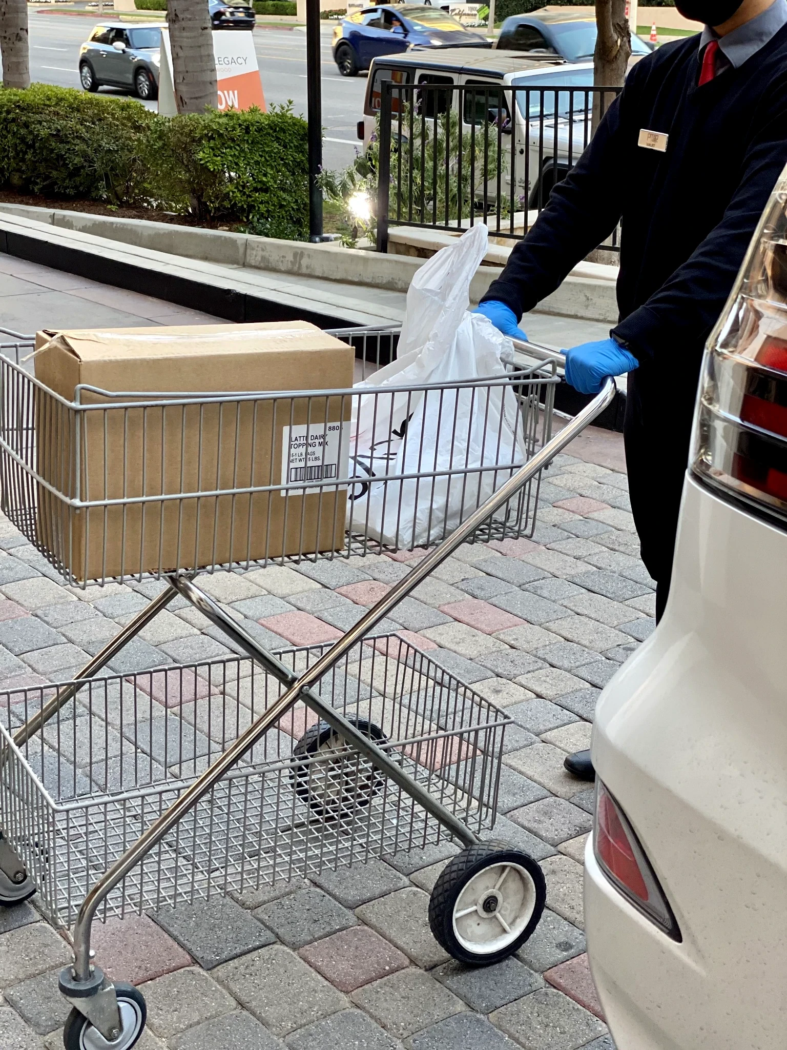 PMSA attendant in dark uniform and blue gloves pushing a shopping cart with packages next to a resident vehicle — Legacy at Westwood