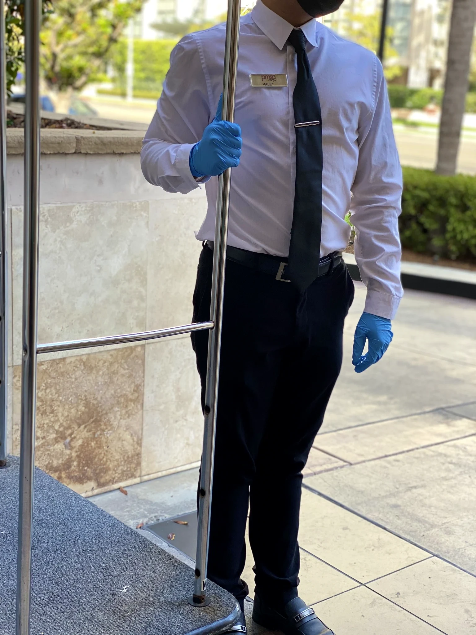 PMSA attendant in white shirt and black tie holding open a car door at a restaurant entrance