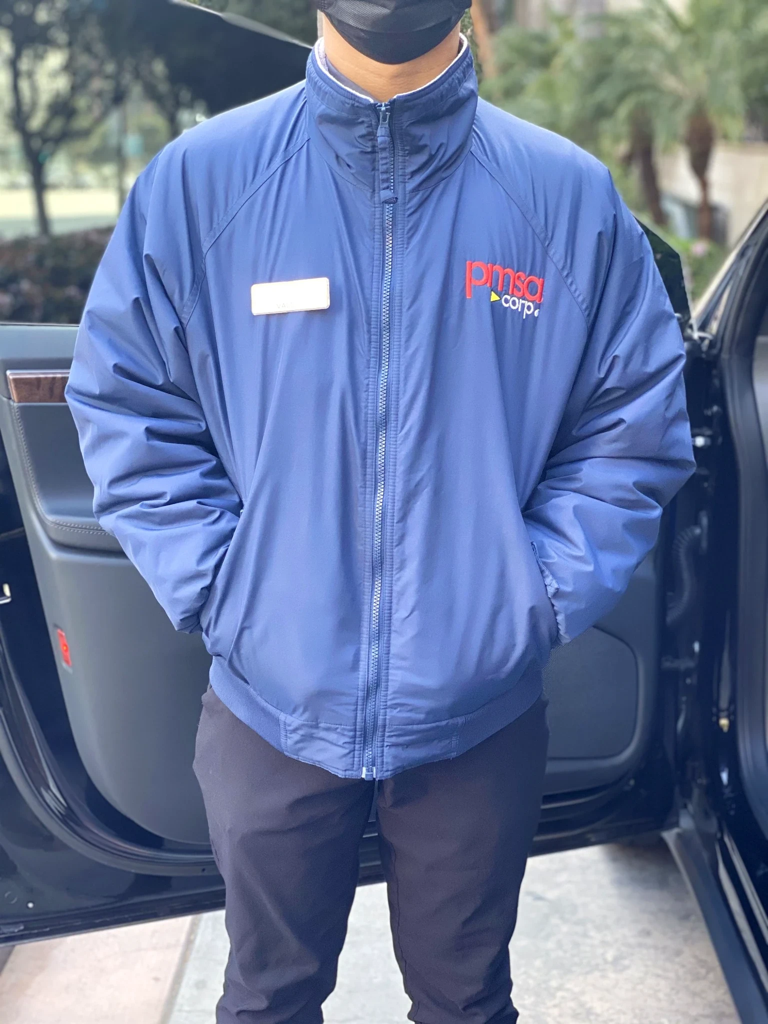 PMSA attendant in branded blue jacket and name badge standing next to an open car door
