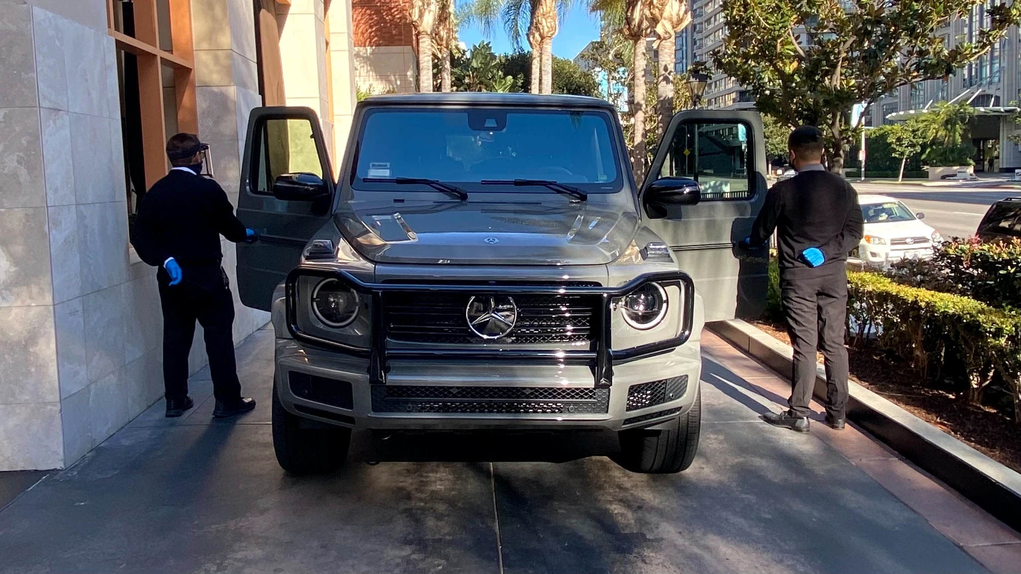 Two PMSA attendants simultaneously opening both doors of a Mercedes G-Wagon at a luxury building entrance