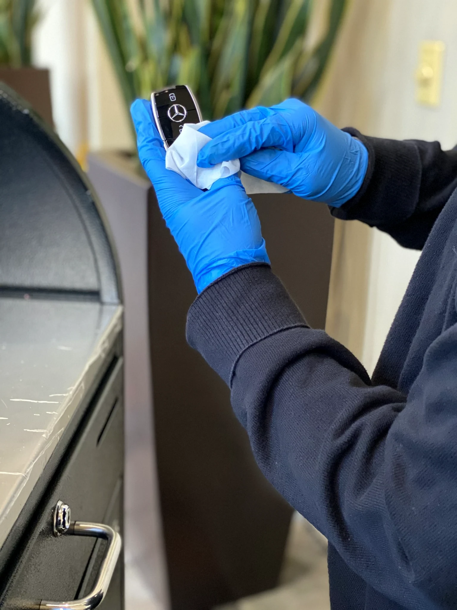 Blue-gloved hands wiping a Mercedes key fob with a white cloth at a valet podium