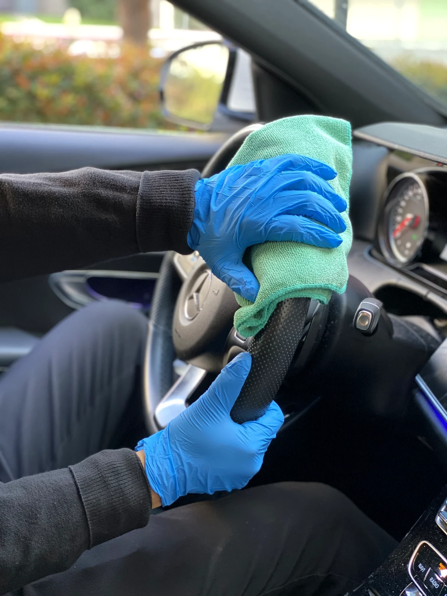 Blue-gloved hands wiping a Lexus steering wheel with a green microfiber cloth