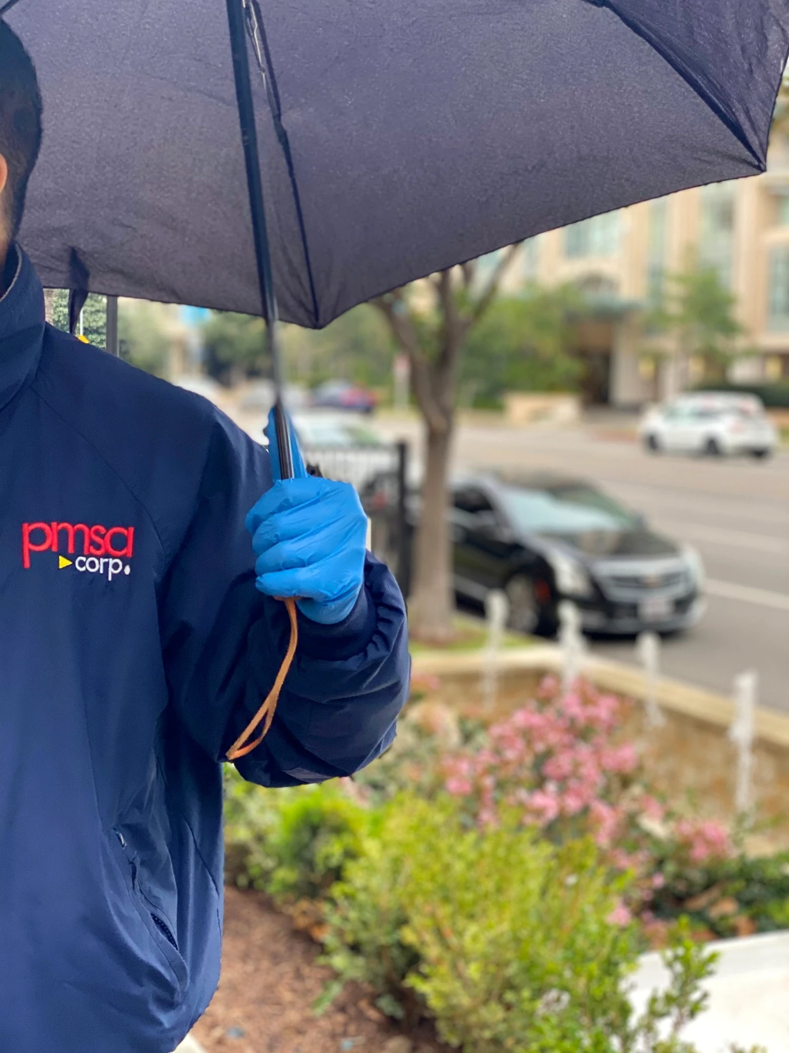 PMSA attendant in branded navy jacket holding umbrella over a car door in the rain